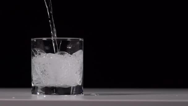 Plan studio d'eau coulant dans du verre transparent sur une table blanche sur fond noir. Super ralenti. Gros plan 