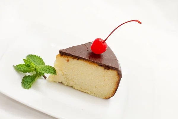cheese cake covered with chocolate icing with mint and cherry on the plate