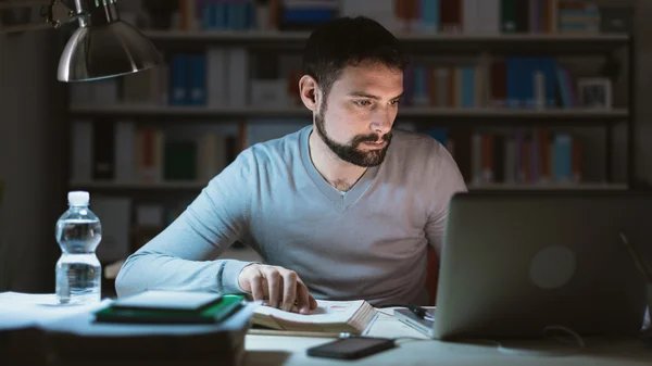 Ung man sitter vid skrivbord, arbetar övertid — Stockfoto