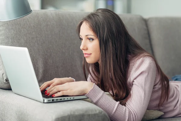 Girl lying on the sofa and using a laptop — Stock Photo, Image