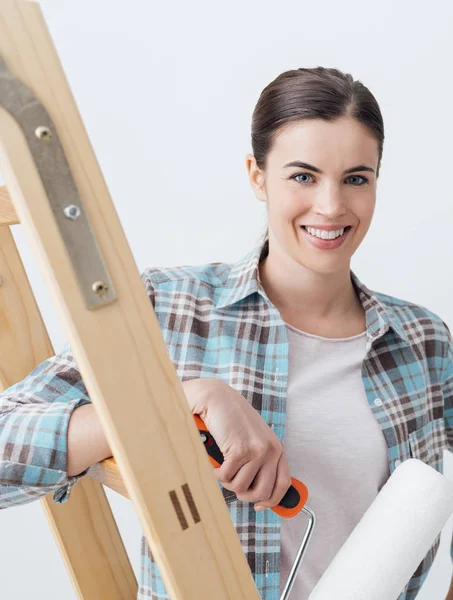 Mujer sosteniendo rodillo de pintura en escalera — Foto de Stock