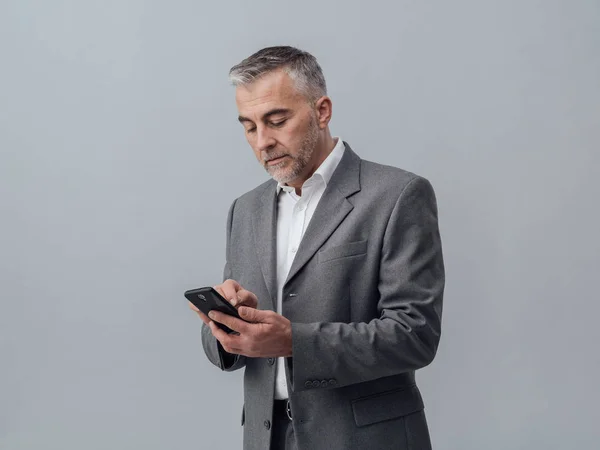 Självsäker mogen affärsman textning med smartphone — Stockfoto