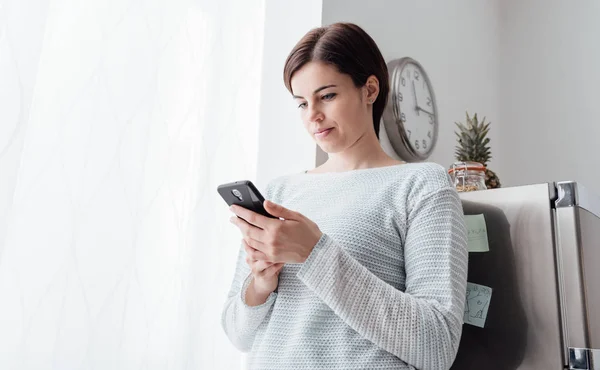 Woman texting in kitchen — Stock Photo, Image