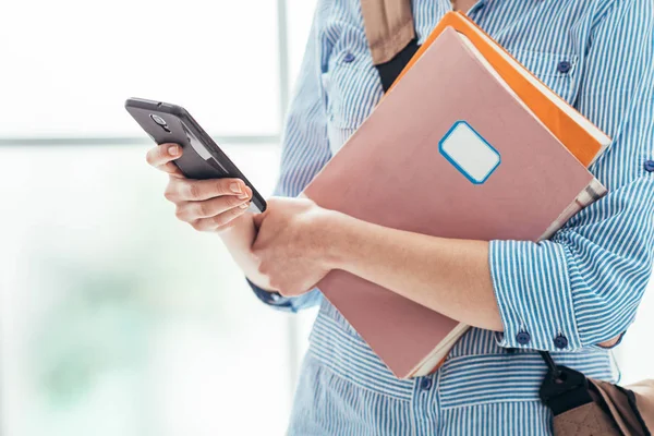 Estudiante sosteniendo cuadernos y mensajes de texto con teléfono inteligente —  Fotos de Stock