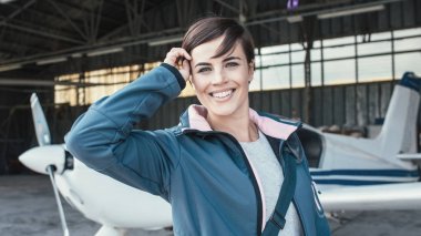 female pilot posing in airport hangar clipart