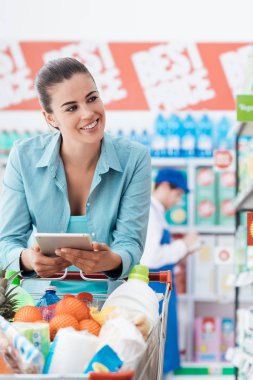 Süpermarkette alışveriş kadın o alışveriş sepeti yaslanmış ve onun tablet, teknoloji ve perakende kavramı üzerinde mobil uygulamalar kullanma