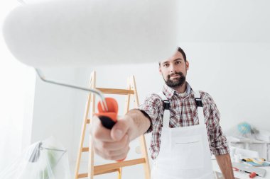 Gülümseyen çalışma profesyonel ressam ve resim, boya silindiri ön plan, ev yenileme ve dekorasyon konsepti