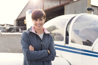 Gülümseyen neşeli kadın hafif uçak ve hangar arka planda havaalanında poz, o genç bir pilot olduğunu