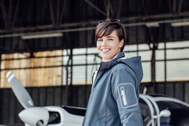 Neşeli gülümseyen genç kadın onun özel küçük uçak, seyahat ve Havacılık konsepti ile Havaalanı hangarda poz