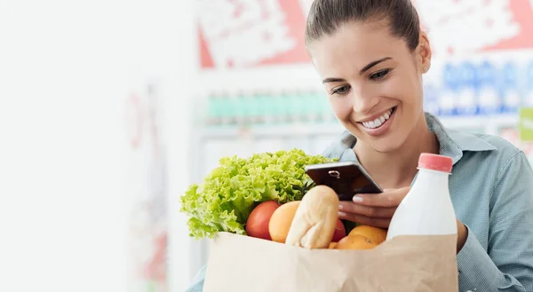 Sonriente Joven Comprando Supermercado Sostiene Una Bolsa Compras Usa Teléfono —  Fotos de Stock