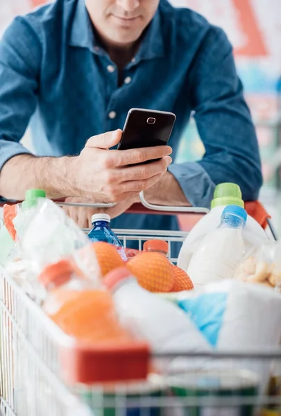 Süpermarkette Alışveriş Adam Alışveriş Sepeti Yaslanmış Cep Telefonuyla Bağlanma — Stok fotoğraf
