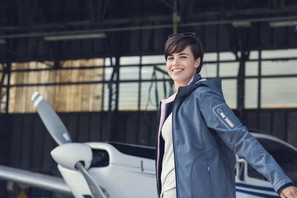 微笑开朗女性试点假扮的机库中与双臂上举像翅膀 螺旋桨飞机的背景 旅行和航空的概念 — 图库照片
