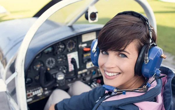Smiling female pilot in the light aircraft cockpit, she is wearing aviator headset and looking at camera