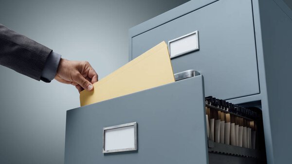 Office clerk searching files in a filing cabinet drawer, business administration and data storage concept