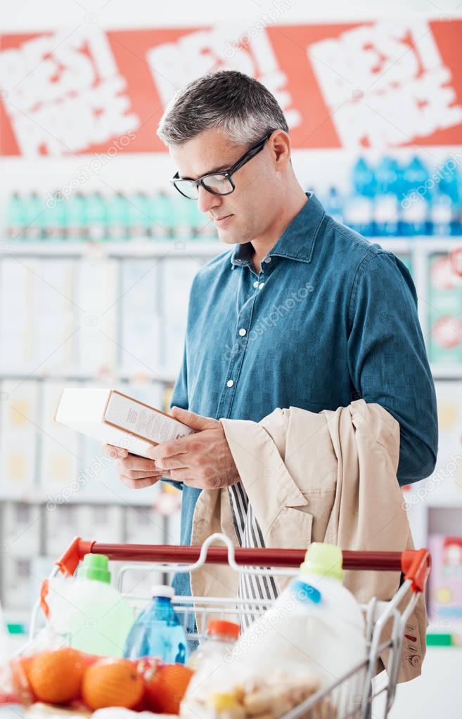 Man doing grocery shopping at the supermarket and reading a food label on a box, shopping and nutrition concept