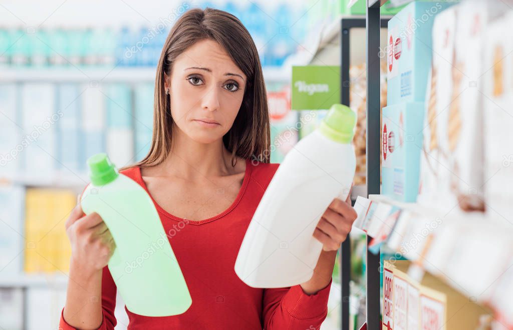 Woman shopping at the supermarket and comparing detergent products, she can't decide which one is the best