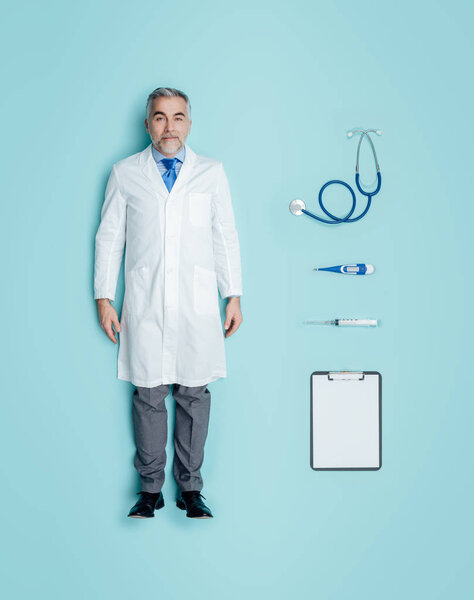 Lifelike male doctor human doll wearing a lab coat and medical equipment accessories, flat lay