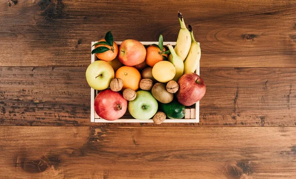 Fresh tasty fruit in a crate and wooden table top view, healthy food concept