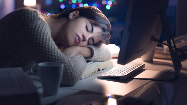 Tired young woman sleeping on the desk late at night, insomnia and exhaustion concept