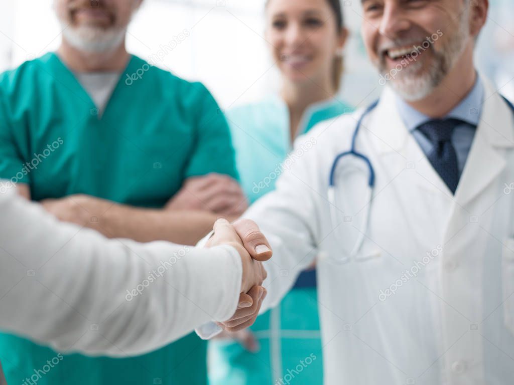 Smiling confident doctor shaking patients hand at the hospital and medical team 