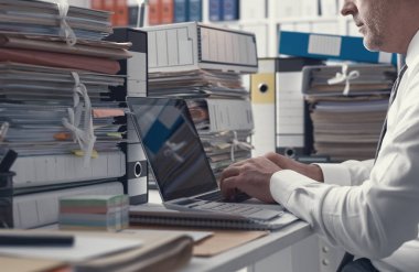 İş o ile bir dizüstü bilgisayar bağlanma ve yazarak executive office ve evrak yığınları ile çalışma,