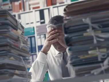 Vurguladı yorgun iş yürütme iş ile aşırı yüklenmiş Office o masanın üzerinde kağıt yığınları vardır
