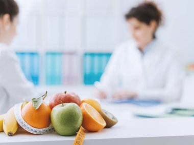 Professional nutritionist meeting a patient in the office and healthy fruits with tape measure on the foreground: healthy eating and diet concept clipart
