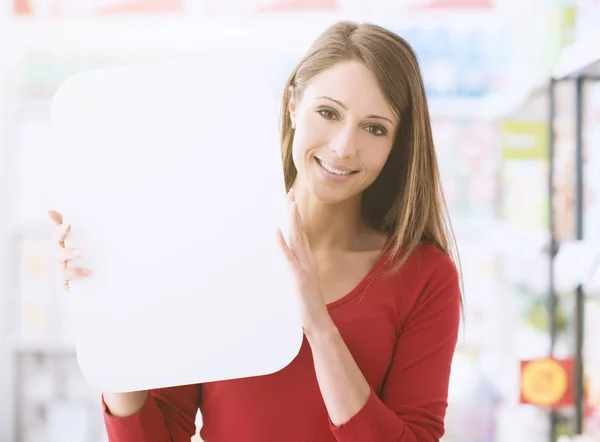 スーパーで女性の笑みを浮かべて 彼女は空白記号 背景に棚を保持しています — ストック写真