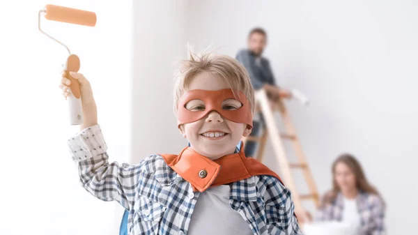 家庭装修他们的家和绘画墙 这个男孩是穿超人服装和控股油漆滚筒 — 图库照片