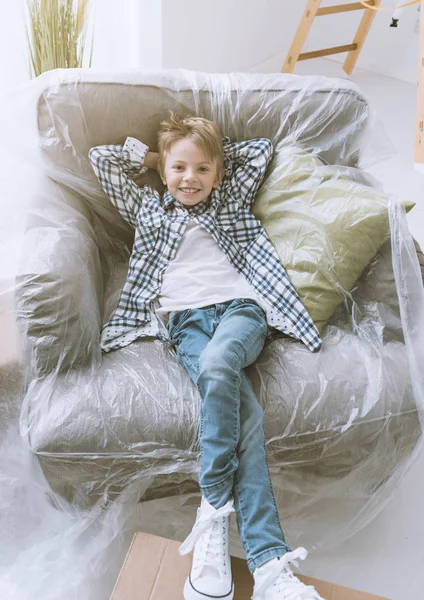 Smiling Happy Boy Relaxing Armchair Covered Protective Plastic Sheet Home — Stock Photo, Image