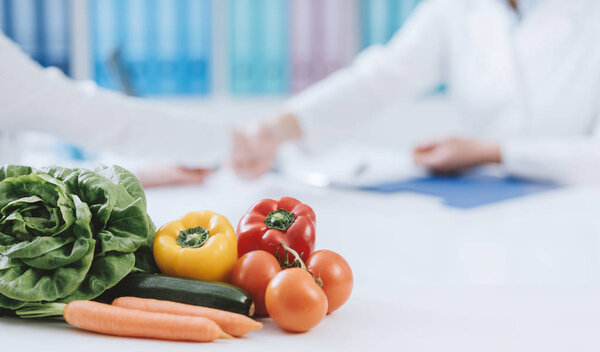 Professional nutritionist working in the office and healthy fresh vegetables on the foreground: diet and health concept
