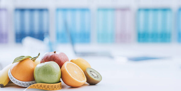 Fresh healthy fruits and tape measure in the nutritionist office: dieting and weight loss concept