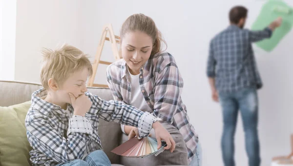 Happy young family renovating and decorating their home, the boy is picking colors swatches with his mother and his father is painting on the background — Stock Image Happy Young Family Renovating Decorating Home Boy Picking Colors Swatches Royalty Free Stock Photos