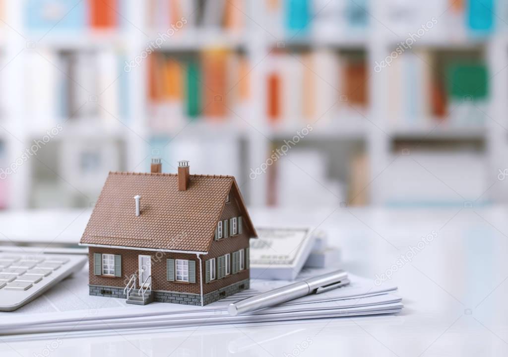 Model house, calculator, cash money and paperwork on a desk: real estate, home loan and investments concept