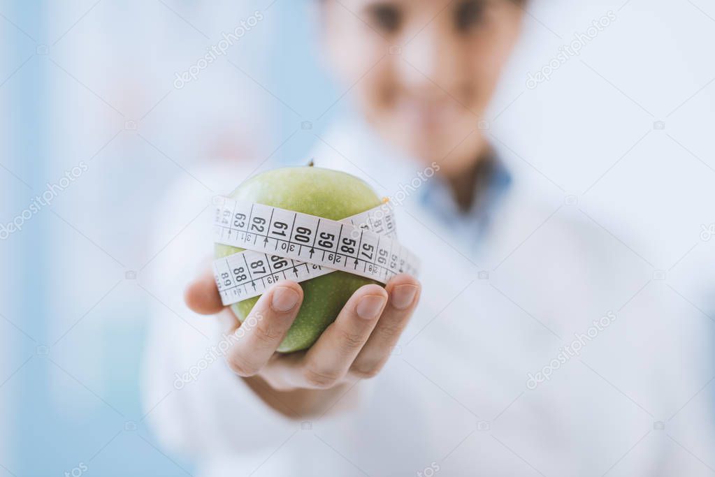 Professional nutritionist holding a fresh apple with tape measure: diet and weight loss concept