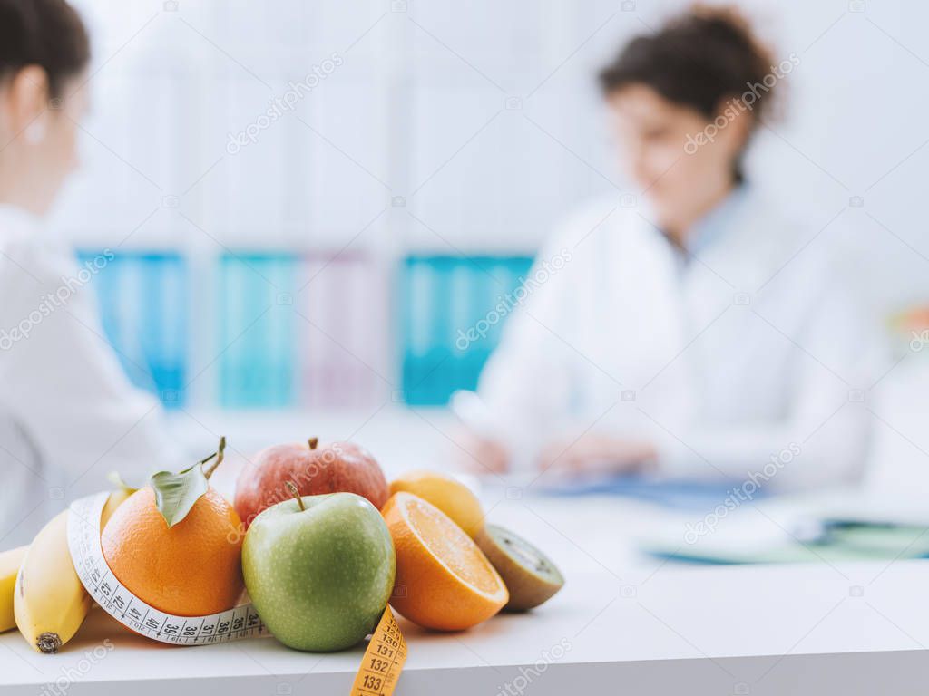 Professional nutritionist meeting a patient in the office and healthy fruits with tape measure on the foreground: healthy eating and diet concept