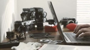 Profesyonel fotoğrafçı onun stüdyosunda çalışma ve çevrimiçi bir dizüstü bilgisayar, vintage film kameraları ve standart lens kameralar üzerinde arka plan kullanarak bağlanma