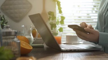 Kahvaltı kadın mutfakta, o ile bir dizüstü bilgisayar bağlanma ve onun Smartphone'da alma