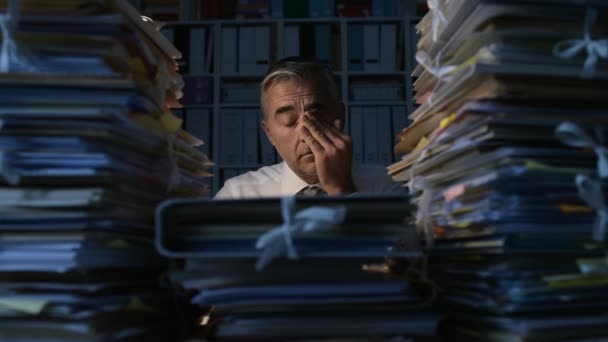 夜遅くまで働くビジネスマンに疲れて 彼は仕事に圧倒され 彼の机が書類でいっぱいです 仕事残業と期限の概念 — ストック動画