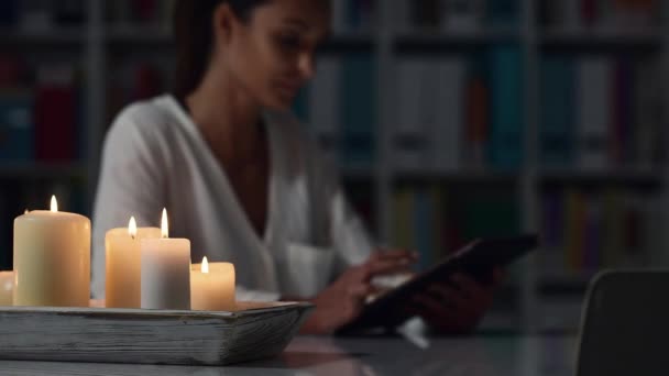 彼女が接続して夜自宅でリラックスできる幸せな女 前景に蝋燭をつけたタブレットとソーシャルネットワー キング — ストック動画