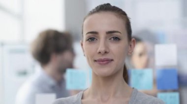 Arka plan üzerinde çalışma ofisi ve iş takım poz genç gülümseyen kadın