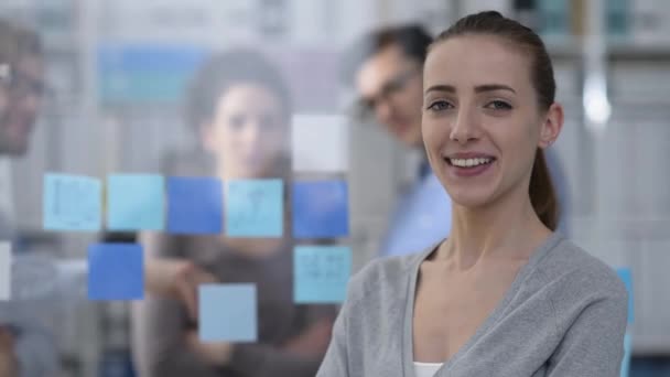 年轻的微笑的妇女摆在办公室和业务团队的背景下工作 — 图库视频影像