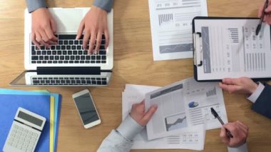 İş takım birlikte masa başında çalışan bir kadın bir dizüstü bilgisayarda yazarak ve erkekler finansal raporlar, eller üstten görünüm inceleyerek