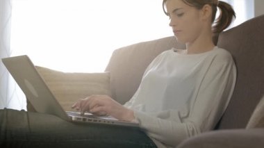 Evde kanepede oturan adlı genç çekici kadın o rahatlatıcı, bir dizüstü bilgisayarda yazarak ve Internet'e bağlanma