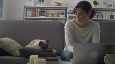 Evde kanepede oturan adlı genç kadın, o çalışma ile bir dizüstü bilgisayar ve onun yanında uyuyan güzel birman kedisi sarılma