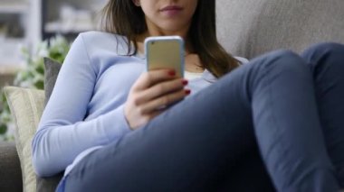 Kanepede yatan ve onun smartphone telefon görüşmesiyle sahip genç kız gülümseyerek