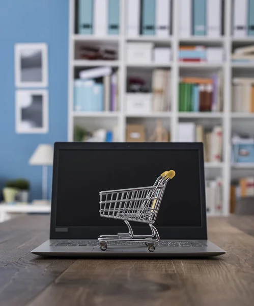 Carrinho de compras em miniatura e laptop em uma mesa — Fotografia de Stock