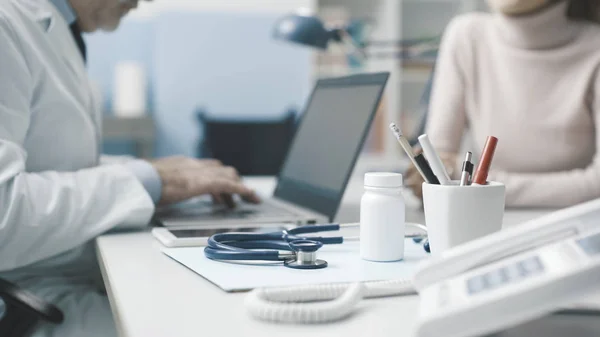 Dokter praat met een patiënt en typt met zijn laptop — Stockfoto
