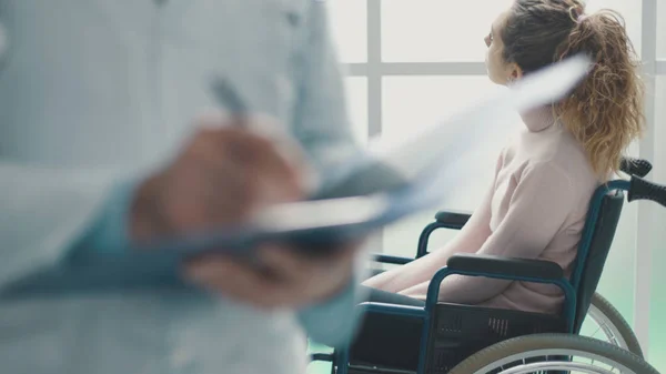 Лікар пише медичні записи та пацієнта в інвалідному візку — стокове фото