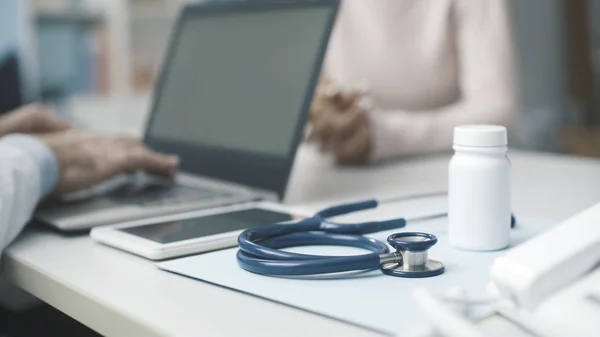 Dokter praat met een patiënt en typt met zijn laptop — Stockfoto